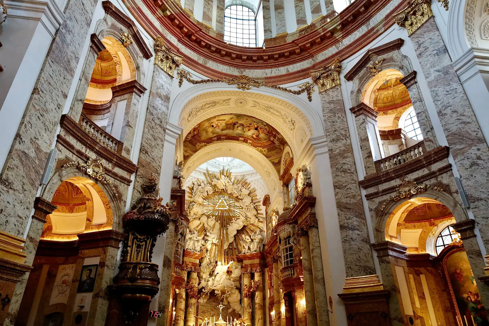 Inside Karlskirche, pale marble pillars rising toward the dome above a gilded high altar