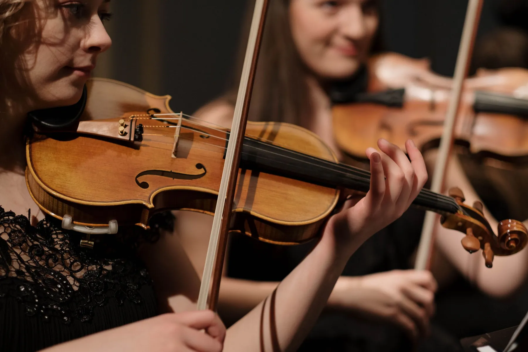 Two violinists mid-phrase with bows raised during a classical concert